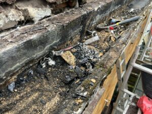 A view of concrete guttering being cleared of old materials and debris, with tools and scaffolding in place.