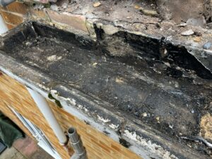 Close-up of broken lining and debris being removed from the concrete gutter, showing decay and damage.
