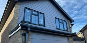 House with new grey cladding, white fascia, soffit and black guttering under a clear blue sky